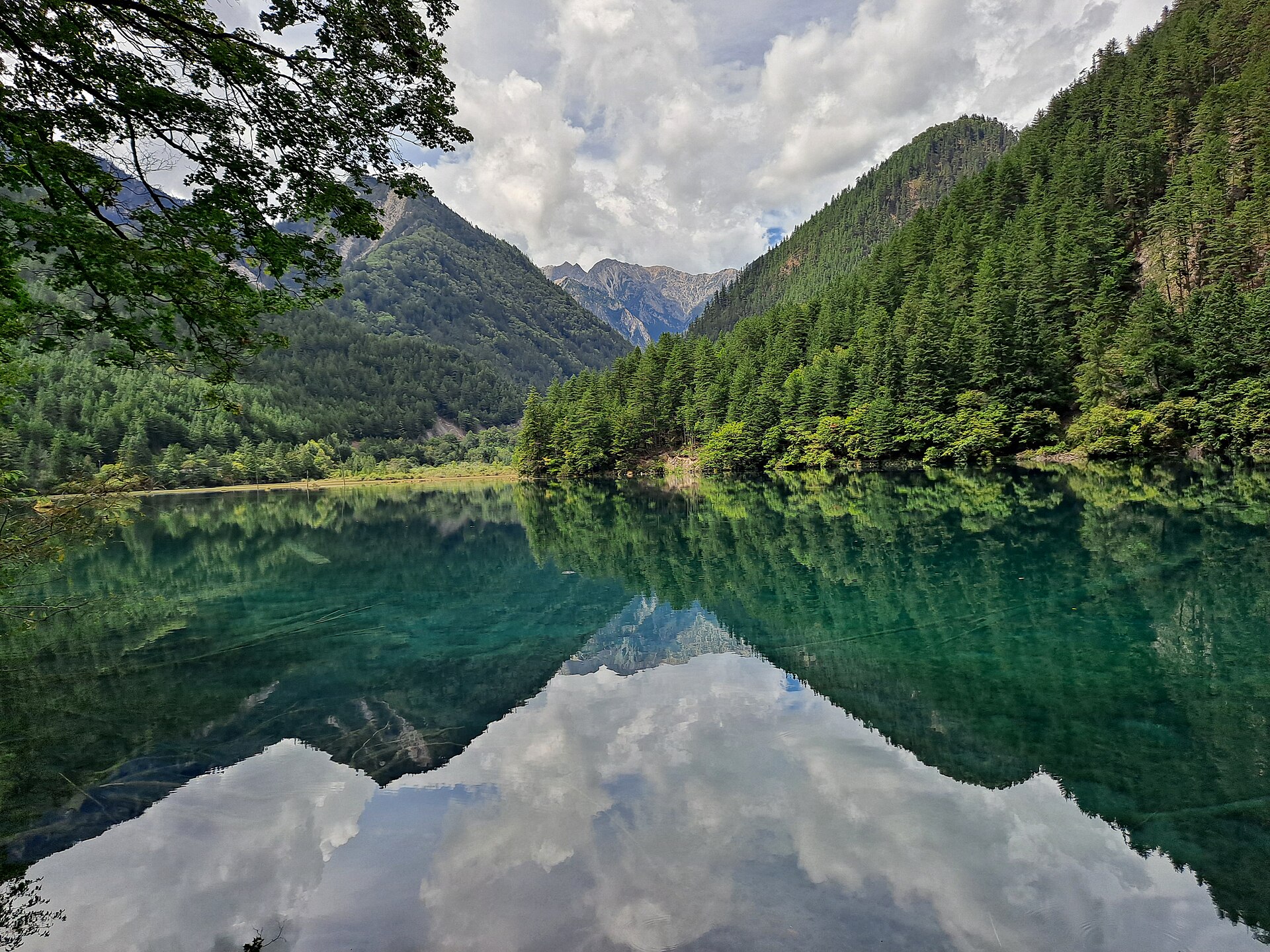 Forested mountains and clouds reflect on the still surface of Mirror Lake in Jiuzhaigou.