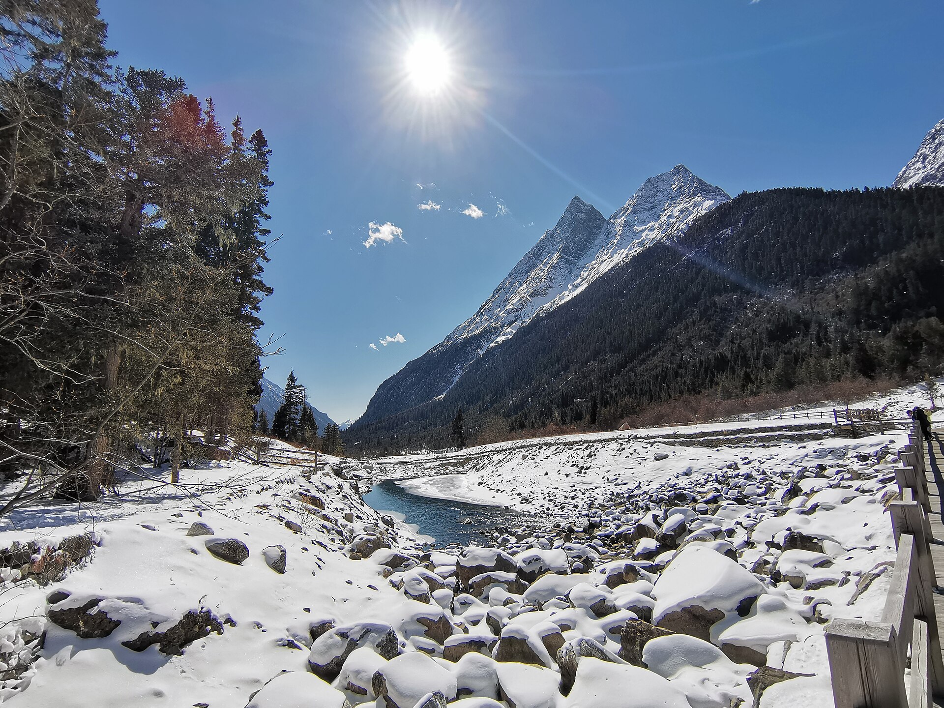 A wooden visitor boardwalk follows a snow-covered river valley in Shuangqiao Valley, Mount Siguniang.